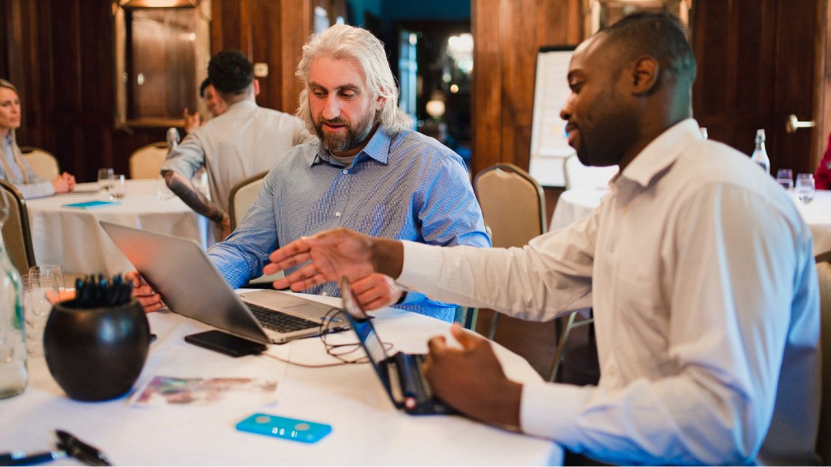 two men sitting at restaurant conversing staring at laptop