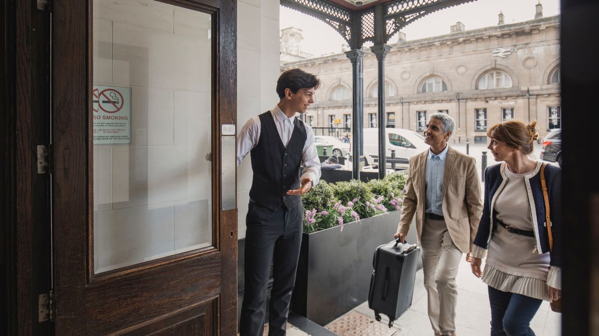 Hotel male personel smiling and welcoming male and female couple into hotel.